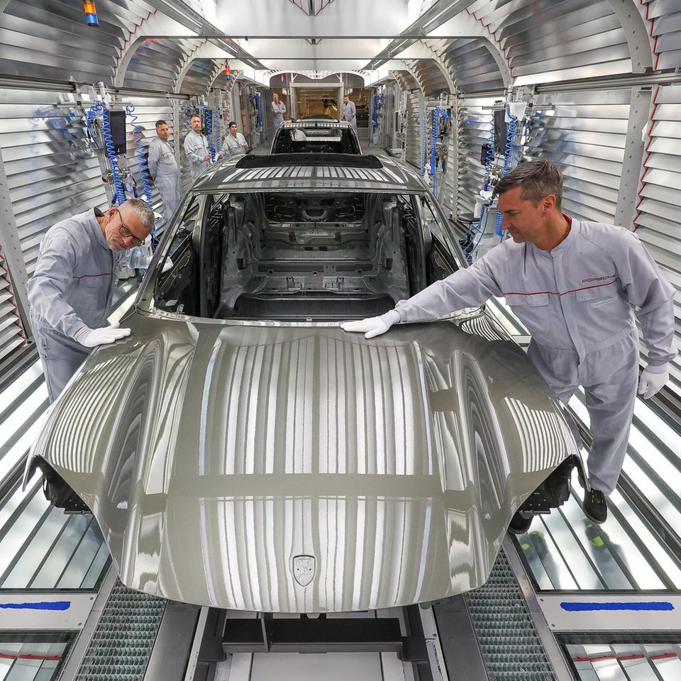 Porsche-Mitarbeiter prüfen in der Lackiererei den Lack der Karosserie eines Porsche Macan im Werk Leipzig
