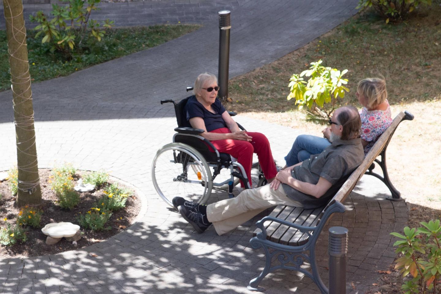 Bewohner des Alfred Delp-Hauses sitzen im Schatten eines Baumes auf einer Bank